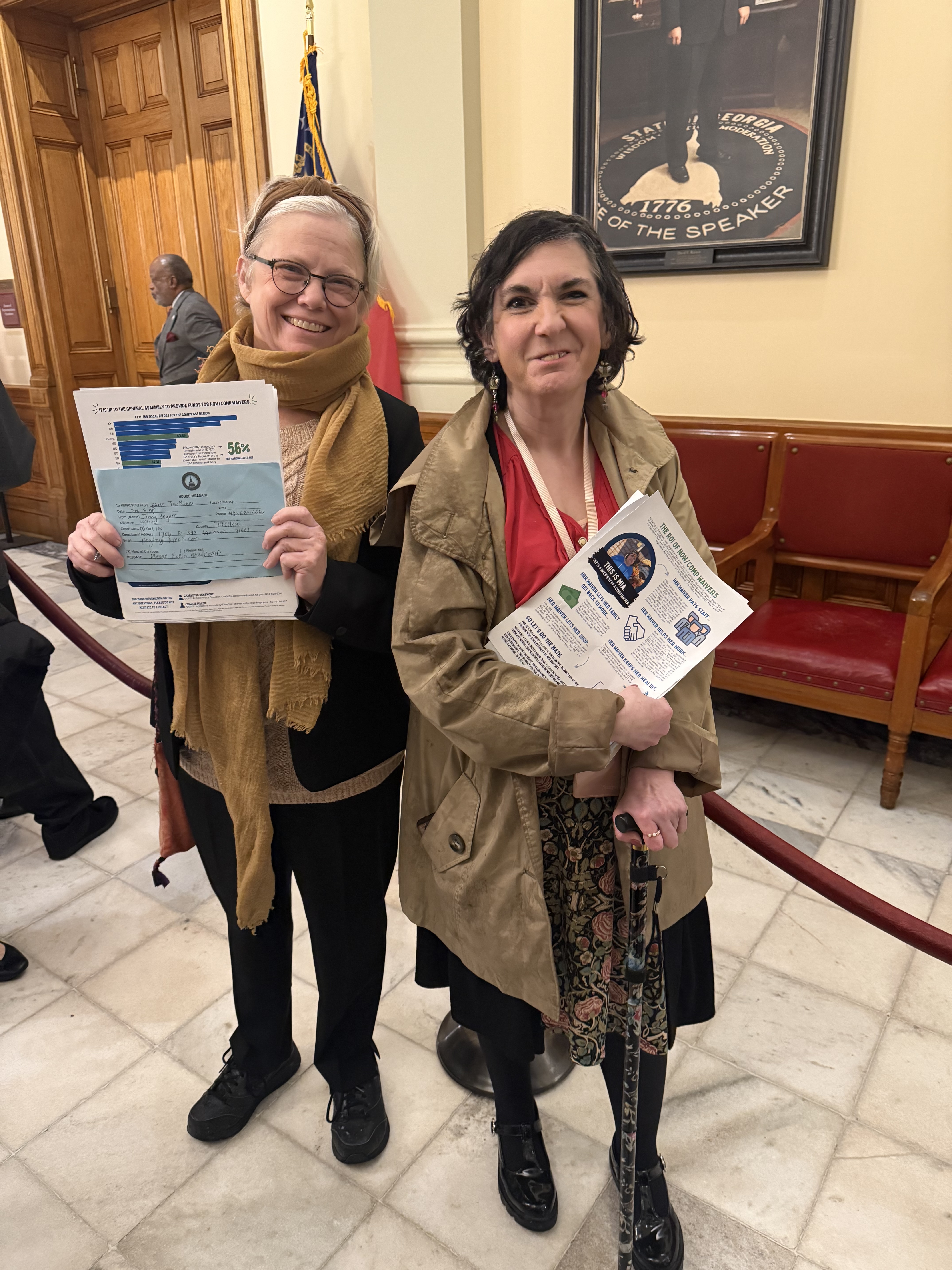 Two women standing next to each other holding sheets of paper.