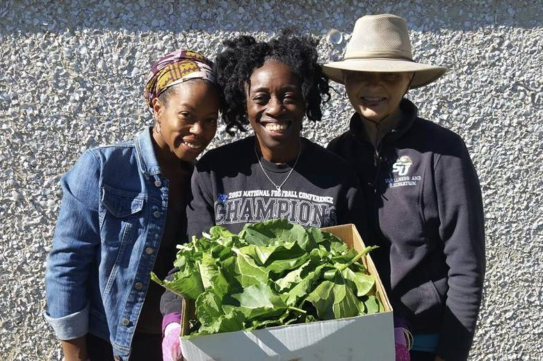 3 women, 2 Black and one white, hold box of lettuce