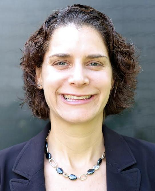 headshot of Alison Barkoff, a young white woman with dark wavy hair smiling at the camera wearing a blue blazer