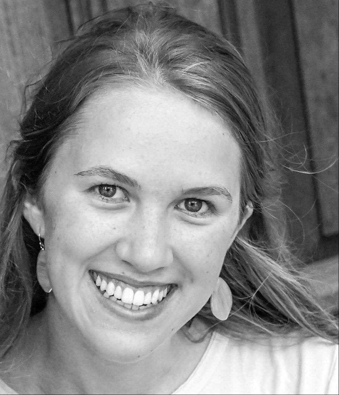 Black and white photo of a white woman with long flowing hair and flower petal earrings. 