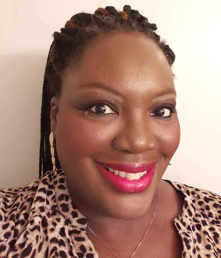 African American woman wearing a cheetah print blouse, red lipstick, gold earrings, and braids in her hair. 