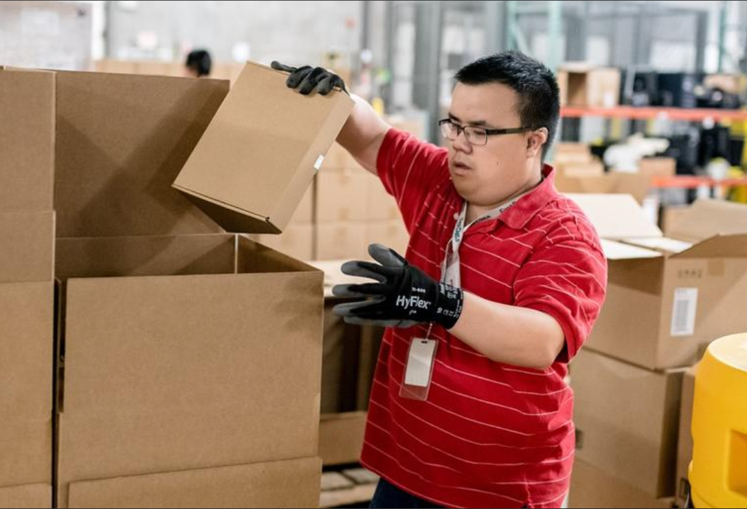 white man with glasses wearing gloves fills boxes in a warehouse